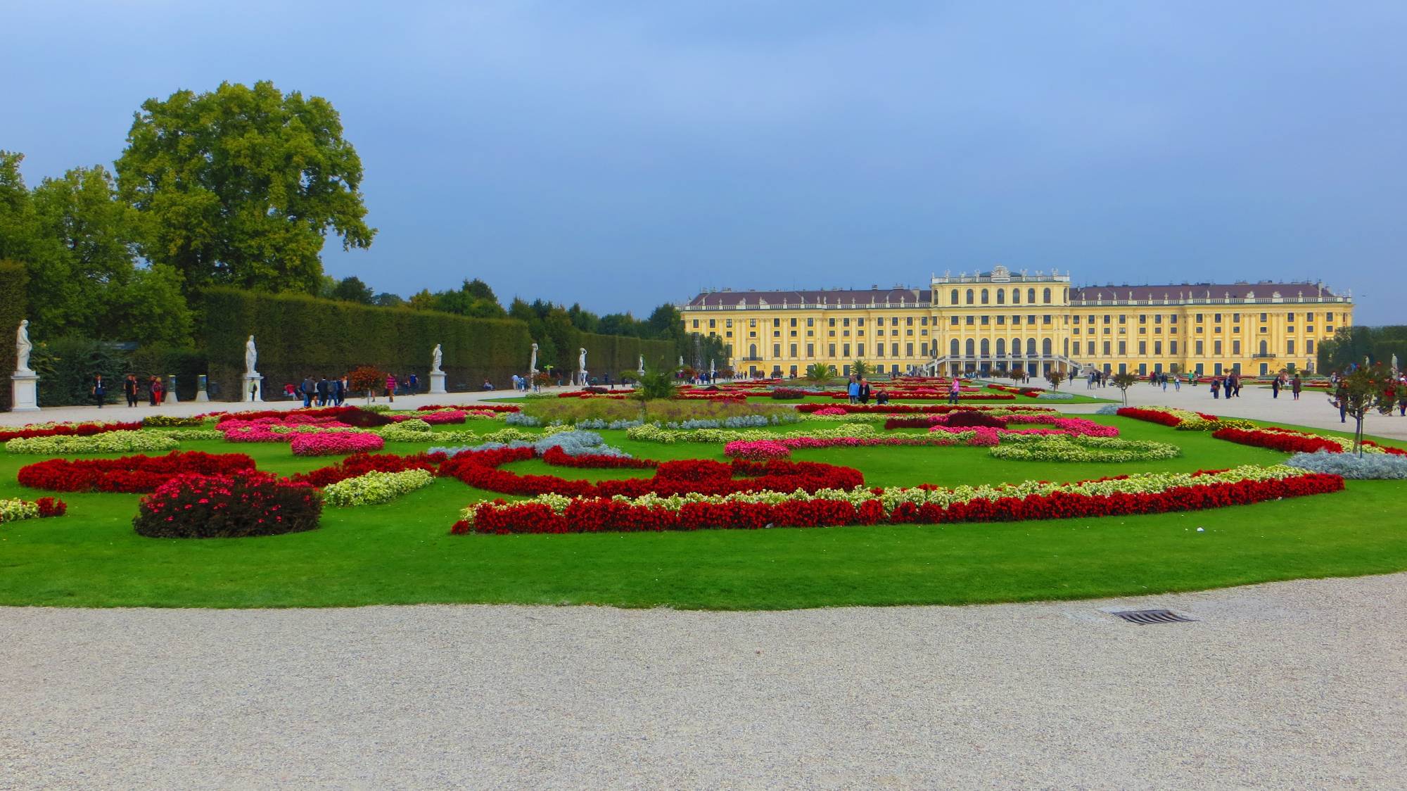 Wide view of the formal gardens of Schönbrunn Palace in Vienna with symmetrical paths and hedges.
