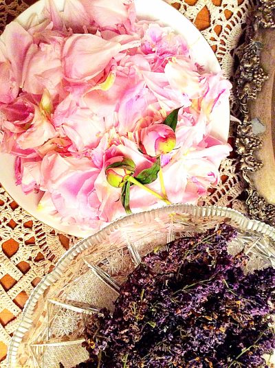 Pink flower petals and dried lavender arranged on plates and cut glass, suggesting scent, memory, and quiet domestic ritual.