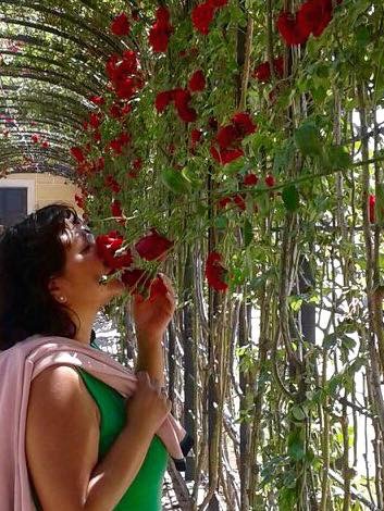 Founder Yolanda Reischer-Bohanec smelling red roses in a garden setting, surrounded by greenery and soft light.