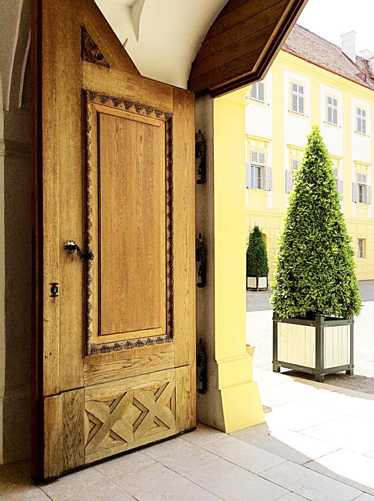 Historic yellow Viennese façade with an arched passageway, clipped trees, and a view through several courtyard openings.