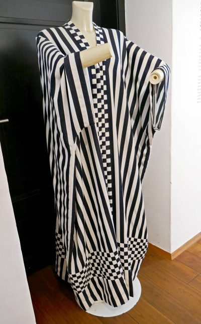 Black-and-white striped dress by Emilie Flöge displayed on a mannequin, with wide flowing sleeves, a loose straight silhouette and checkerboard detailing at the front opening and hem.