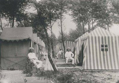 Black-and-white historical photograph of the Gänsehäufel with striped and plain bathing tents arranged in rows among trees, with several visitors seated outside the tents.