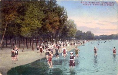Historical colour postcard of the Gänsehäufel family beach in Vienna, with crowds of adults and children in early twentieth-century swimwear standing and bathing along the wooded shore of the Alte Donau.
