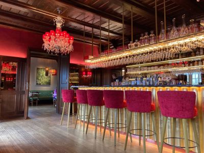 Interior of the renovated Knappenhof bar, with red velvet stools, a brass counter, crystal chandeliers and rows of glasses beneath a dark timber ceiling.