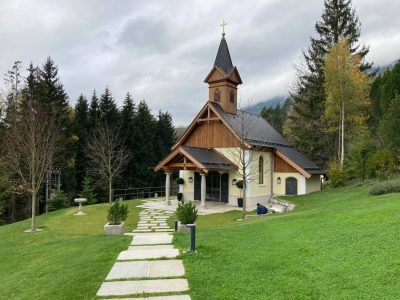 Newly built chapel at the Knappenhof, with timber cladding, a small bell tower and a stone path leading through landscaped grounds.