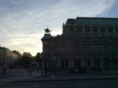 Vienna State Opera seen across the Ringstrasse at dusk, with the building and an equestrian statue silhouetted beneath a luminous evening sky.